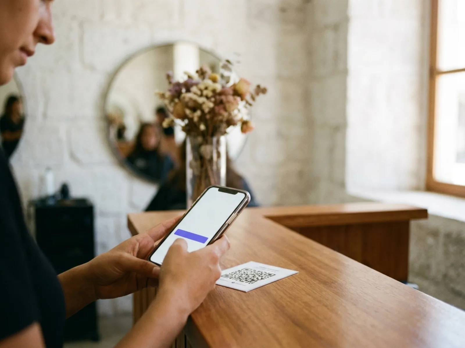 À l'accueil d'un salon, une cliente scanne le QR du comptoir avec son téléphone pour s'inscrire